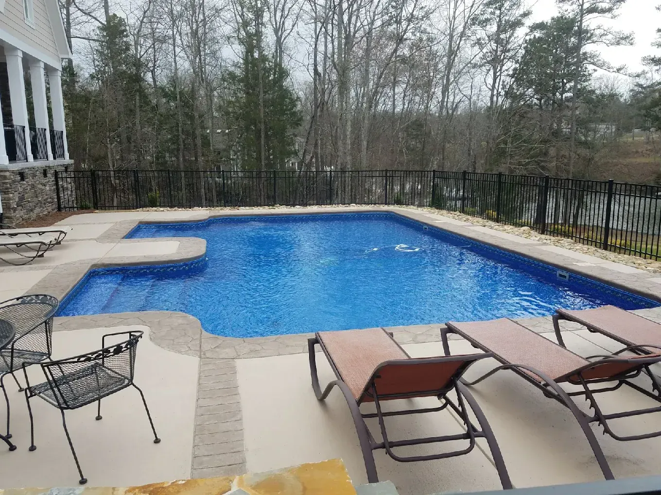 Backyard swimming pool with lounge chairs and patio furniture, surrounded by trees and a fence