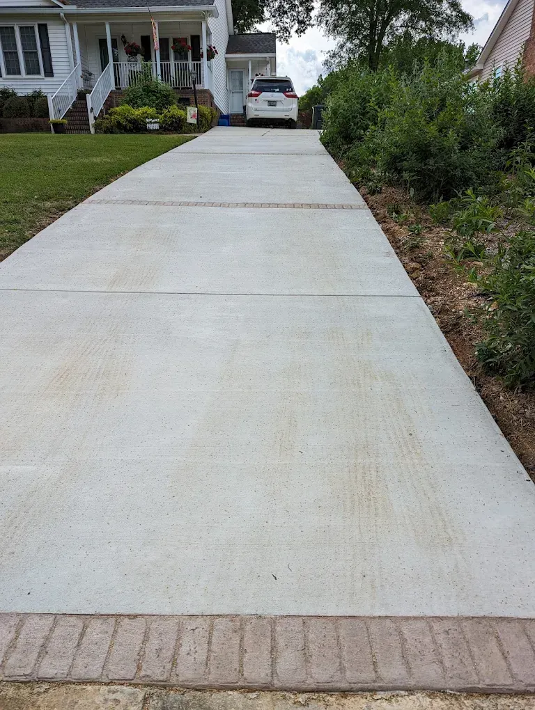 Concrete driveway leading to a house, with a parked car at the top and shrubs along the side.