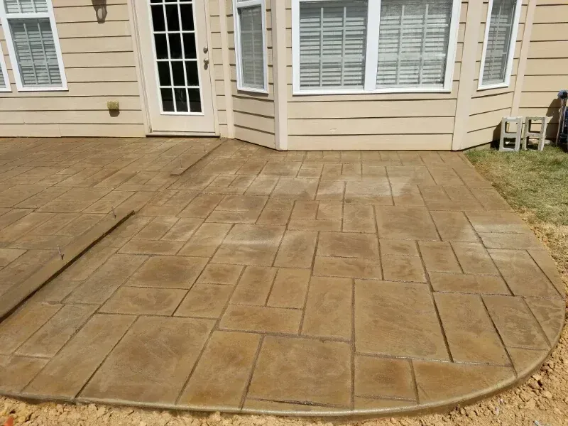 Concrete patio with stamped tan pavers beside a beige house and white French doors