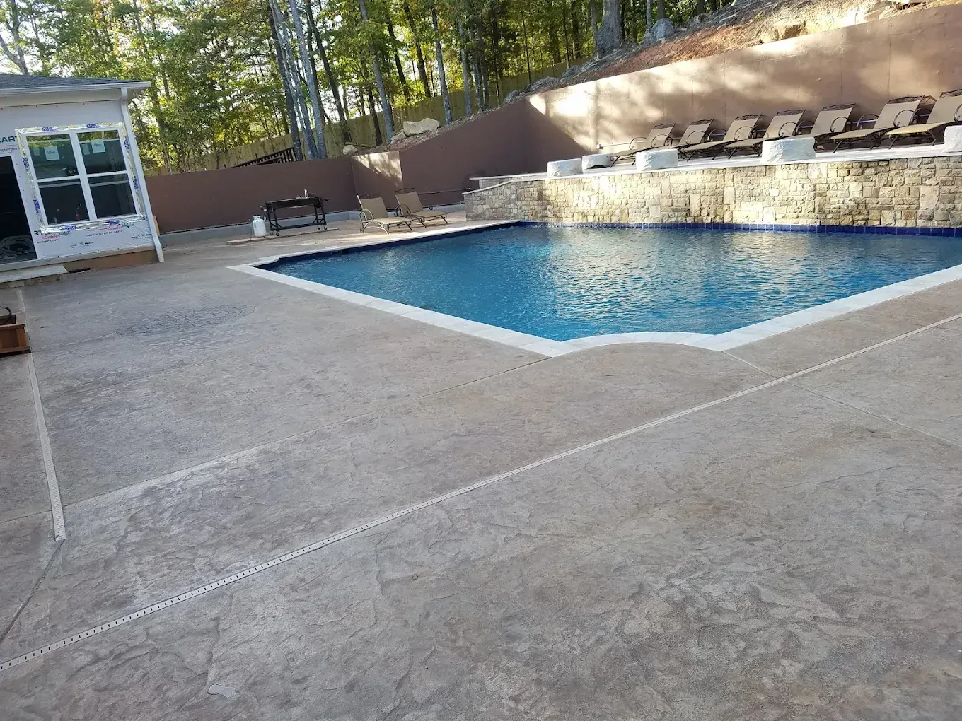 Backyard pool with concrete patio, stone waterfall, and small pool house nearby
