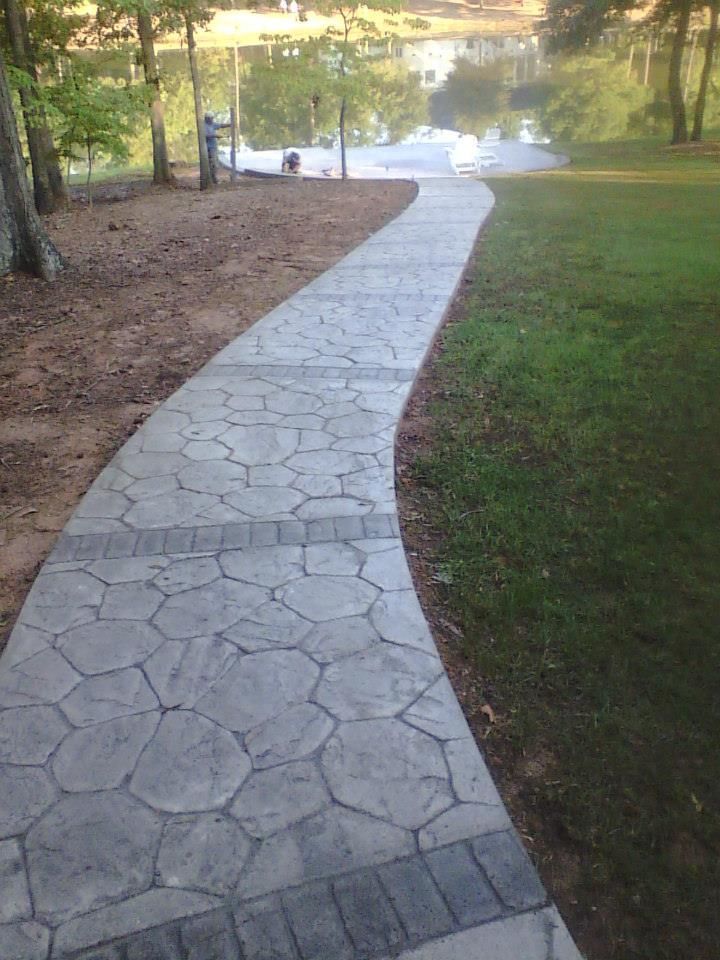 Curved stone walkway leading through a grassy park toward a lake at sunset