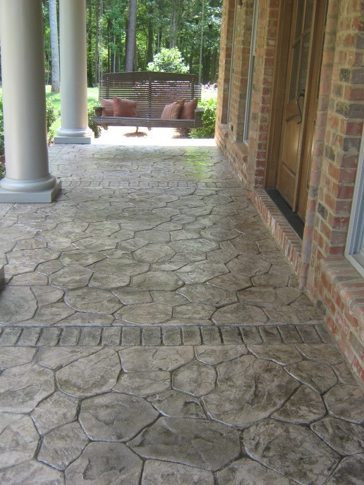 Brick porch with stone-patterned walkway, white columns, and a brick house wall beside a fenced yard.