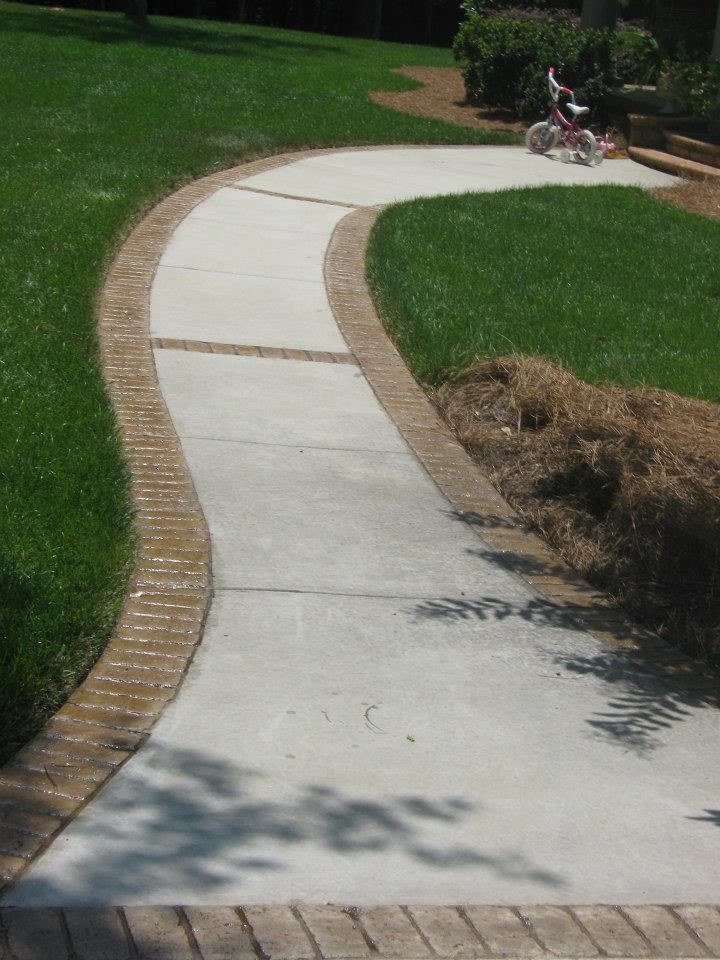 Curving concrete sidewalk through a green park, with a person sitting on a bench in the distance.