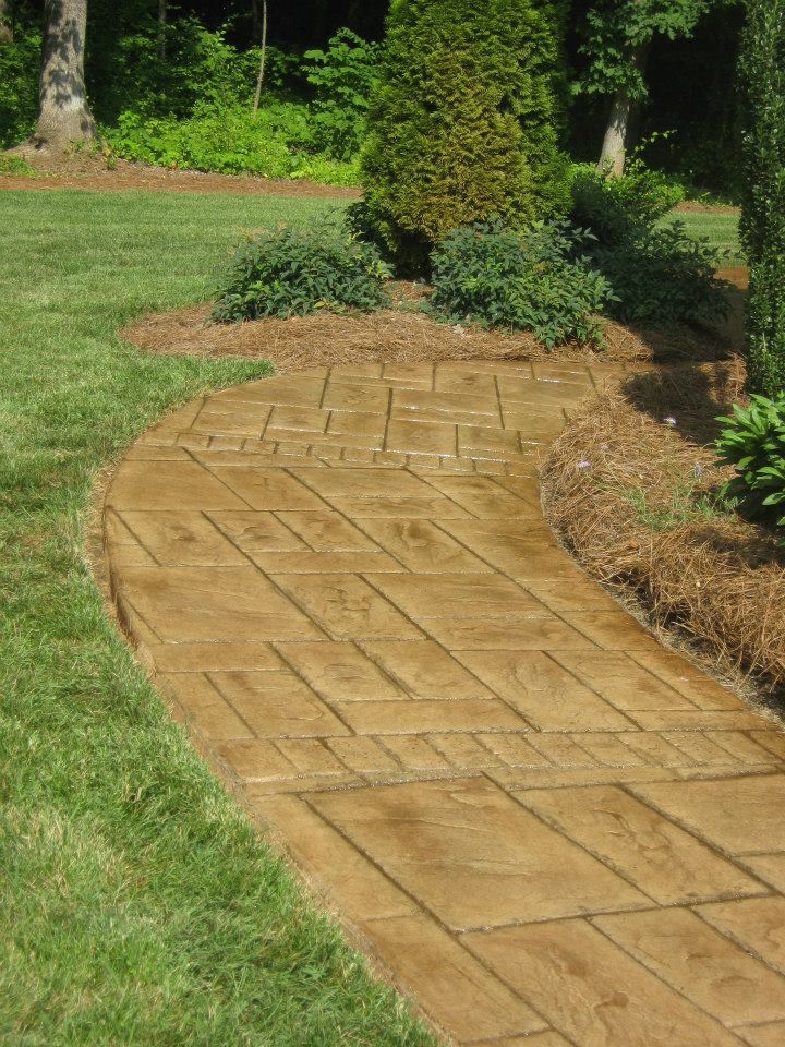 Curved tan stone garden path bordered by green grass and shrubs