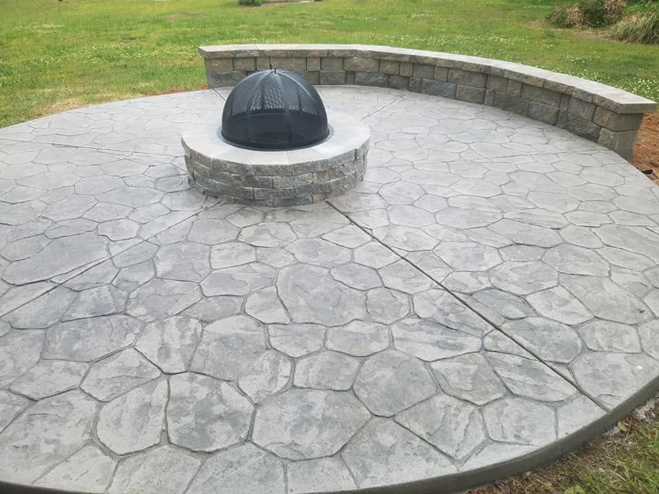 Circular stone patio with a central black dome fire pit in a grassy yard