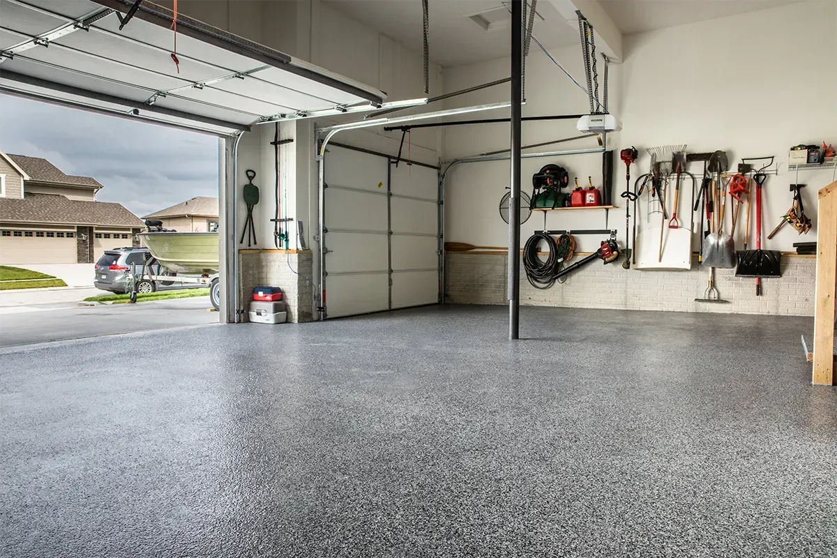 Spacious empty garage with a speckled floor, open doors, and tools mounted on the wall