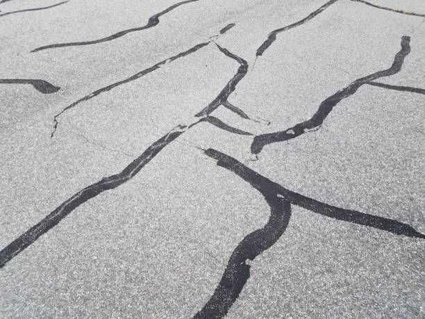 Cracked gray pavement with dark fissures spreading across the surface