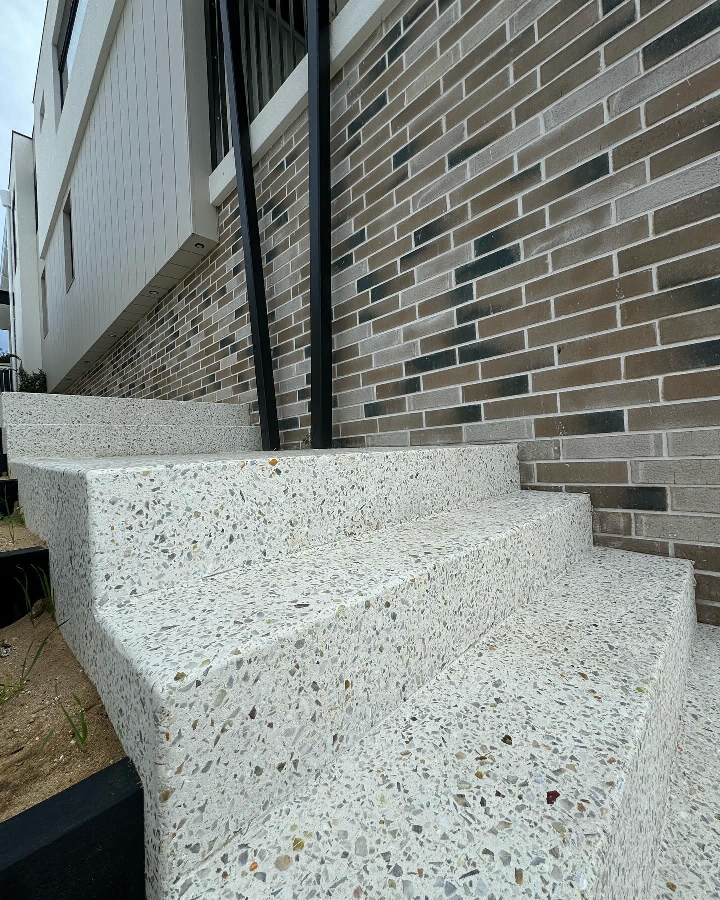 Amber white coloured honed concrete stairs contrasted against dark coloured bricks leading up the side of a home
