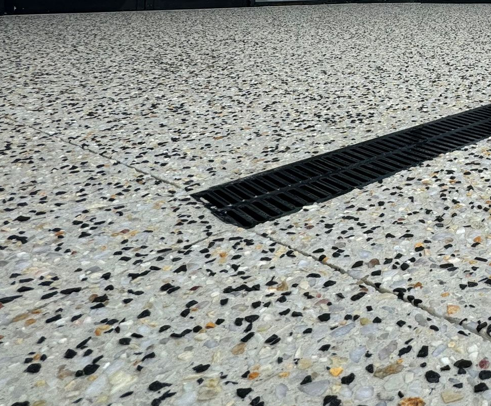 Close up of new exposed aggregate driveway with drainage set within the concrete.