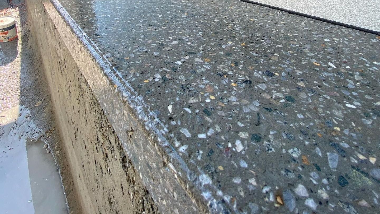 Close-up view of a wet, honed concrete pool edge with embedded aggregate.