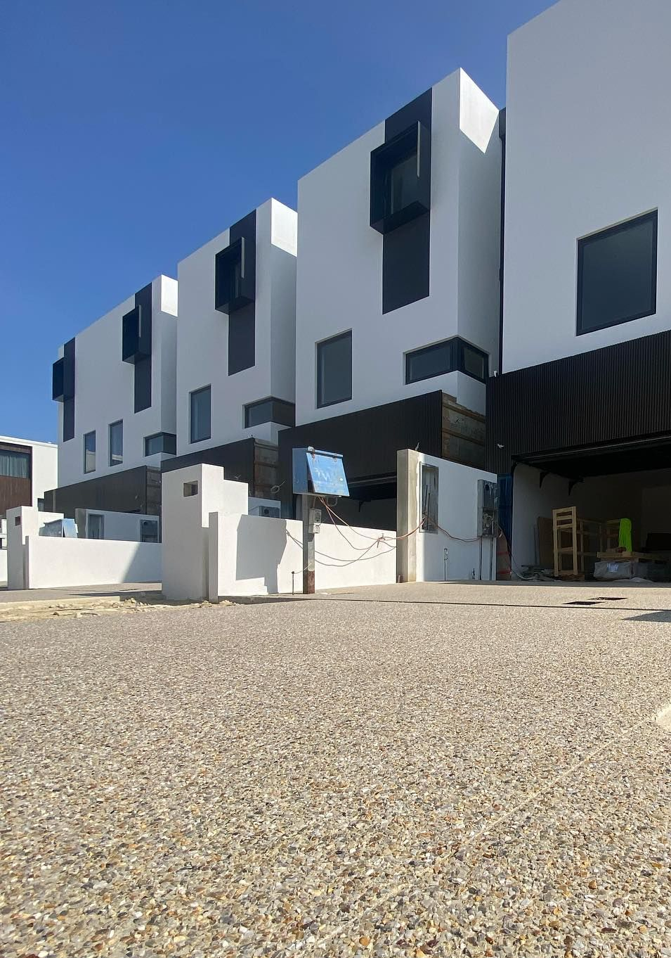 Modern white and black apartment building with exposed aggregate driveway.