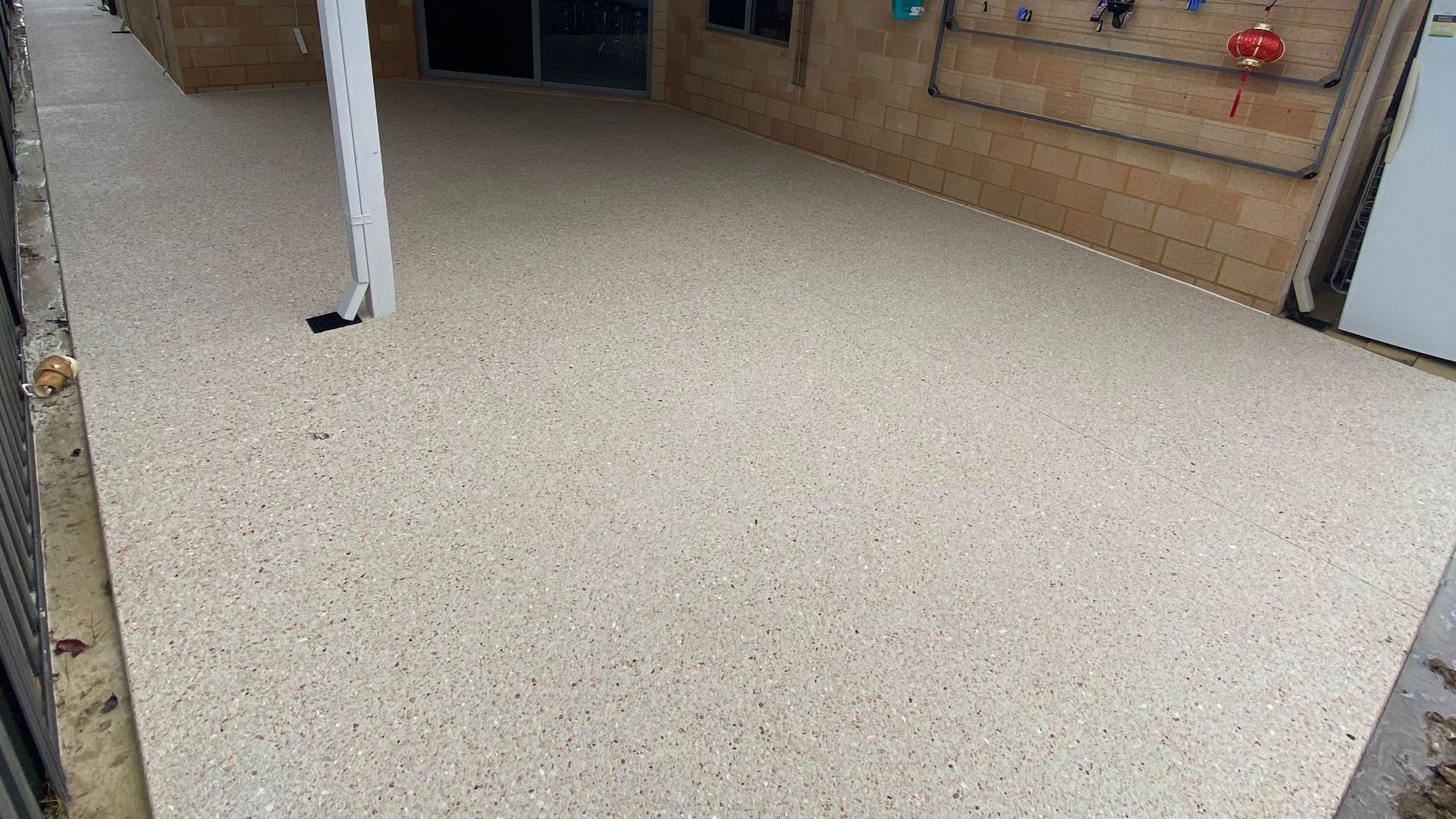 Exposed Aggregate Concrete alfresco with down pipe and white brick house.