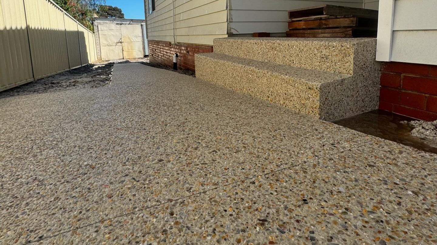 A house with a exposed aggregate concrete walkway and stairs leading up to it.