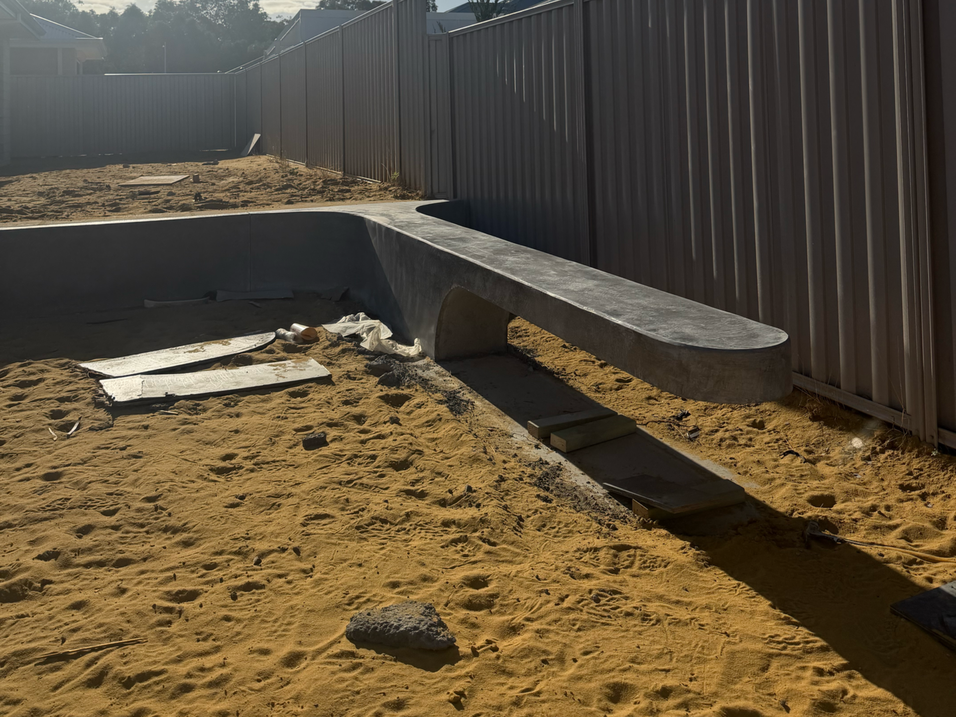 ARCHITECTURAL CONCRETE BENCH SEAT IN BACKYARD OF NEW HOME BUILD WITH YELLOW BICKSAND AND COLOURBOND FENCE
