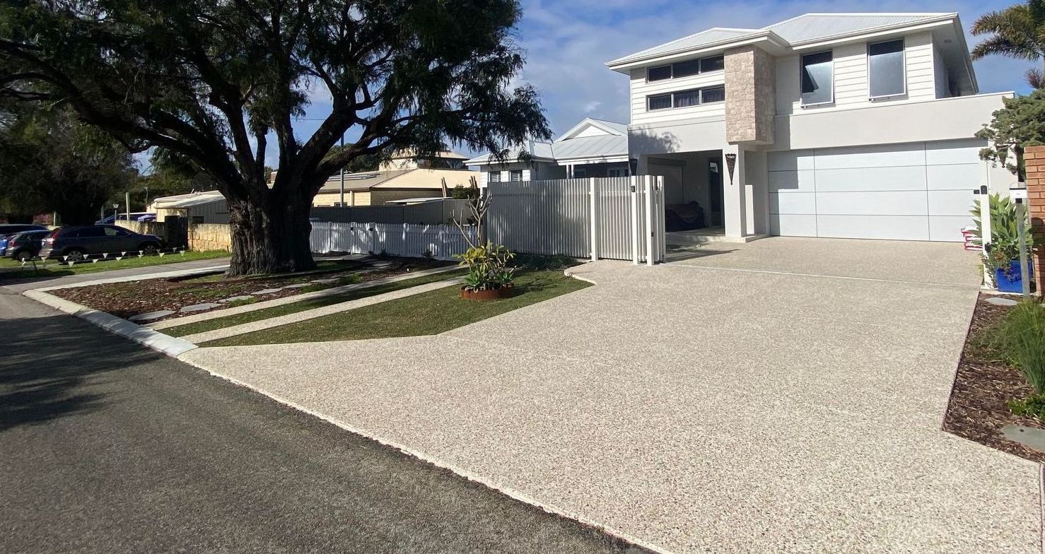Two storey home with large double exposed aggregate driveway and grass.