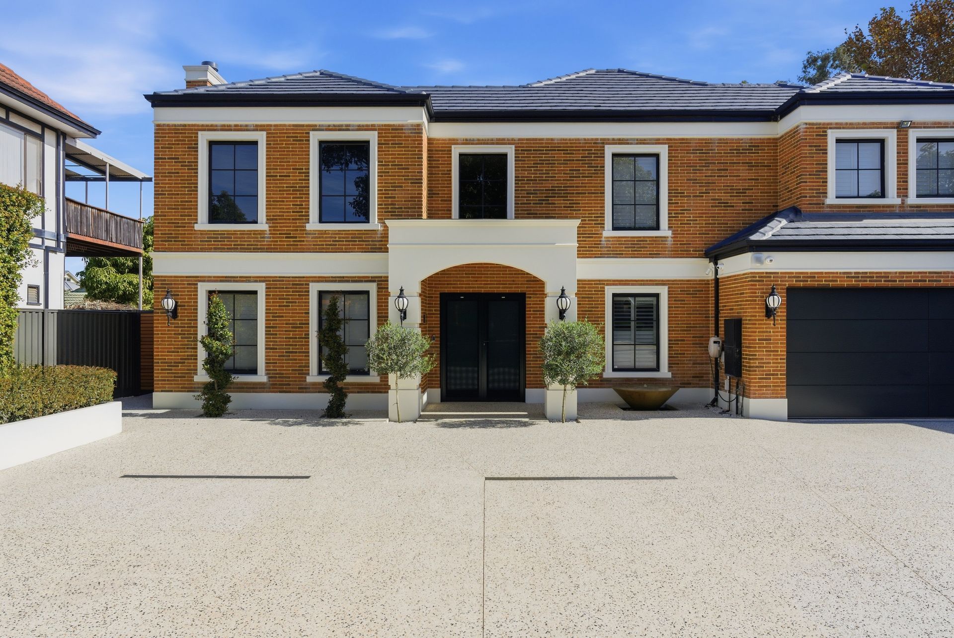 Modern two-story brick house with a black garage, large windows, and a wide concrete driveway
