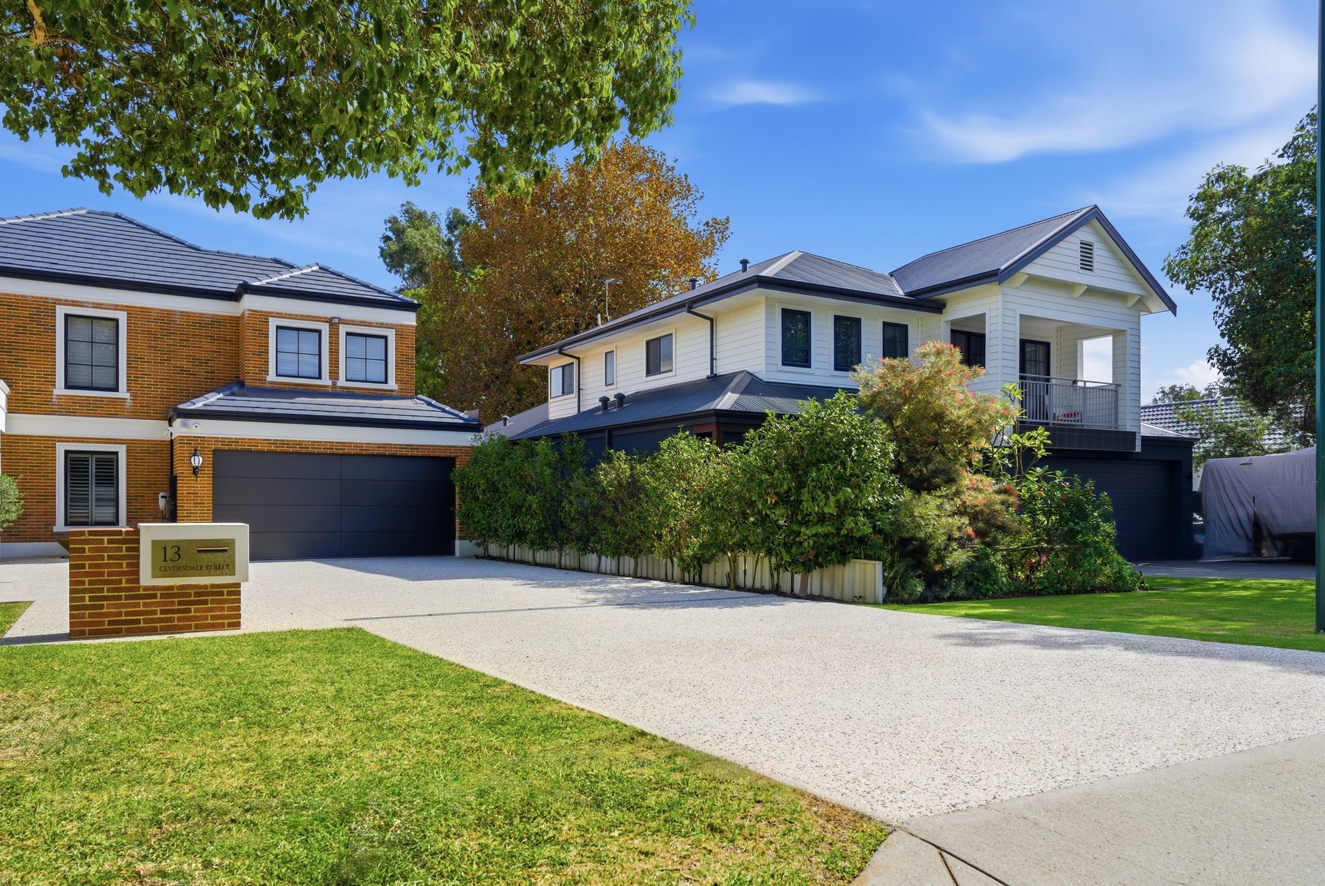 Exposed aggregate concrete driveway with lush green grass at the front of a red brick home with a black roof and black garage doors.