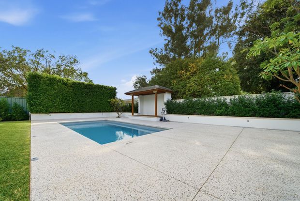Backyard patio with a small blue swimming pool, white decking, and hedges under a clear sky