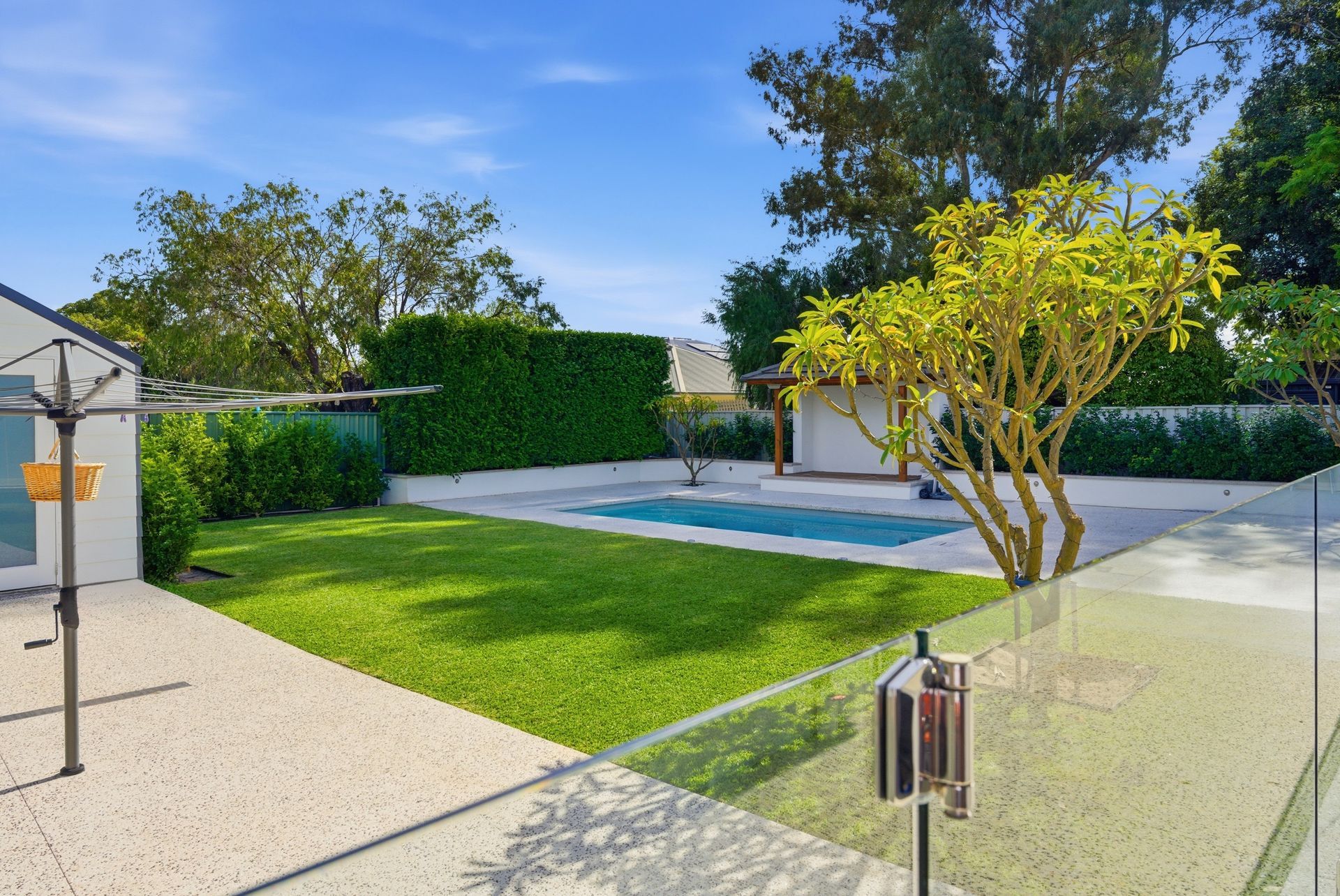 Exposed aggregate pool surrounds with lawn surrounding the pool and lush green landscaping in Perth