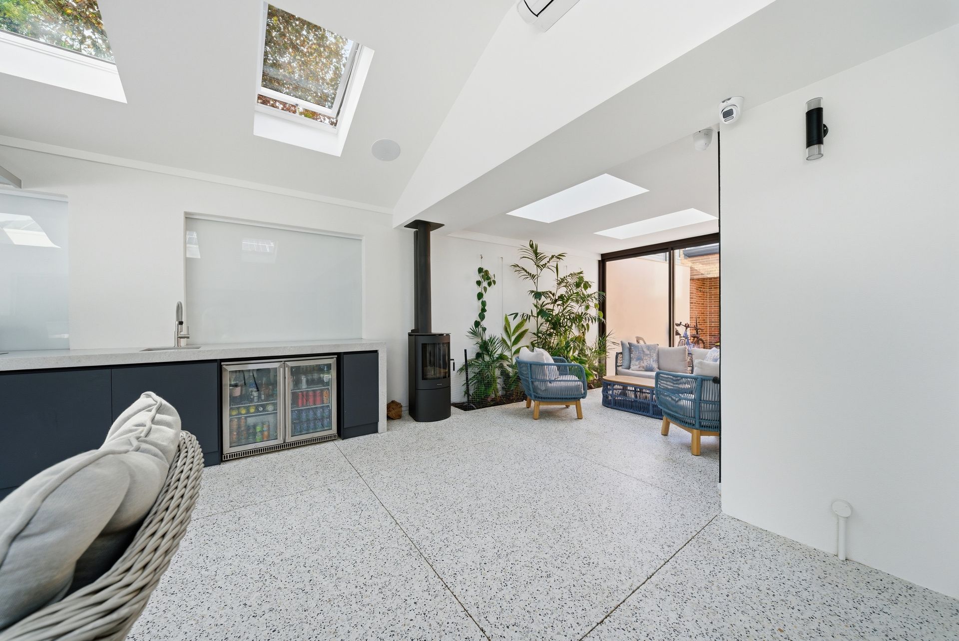 Bright modern alfresco room with white walls, skylights, gray sofa, with honed concrete floor
