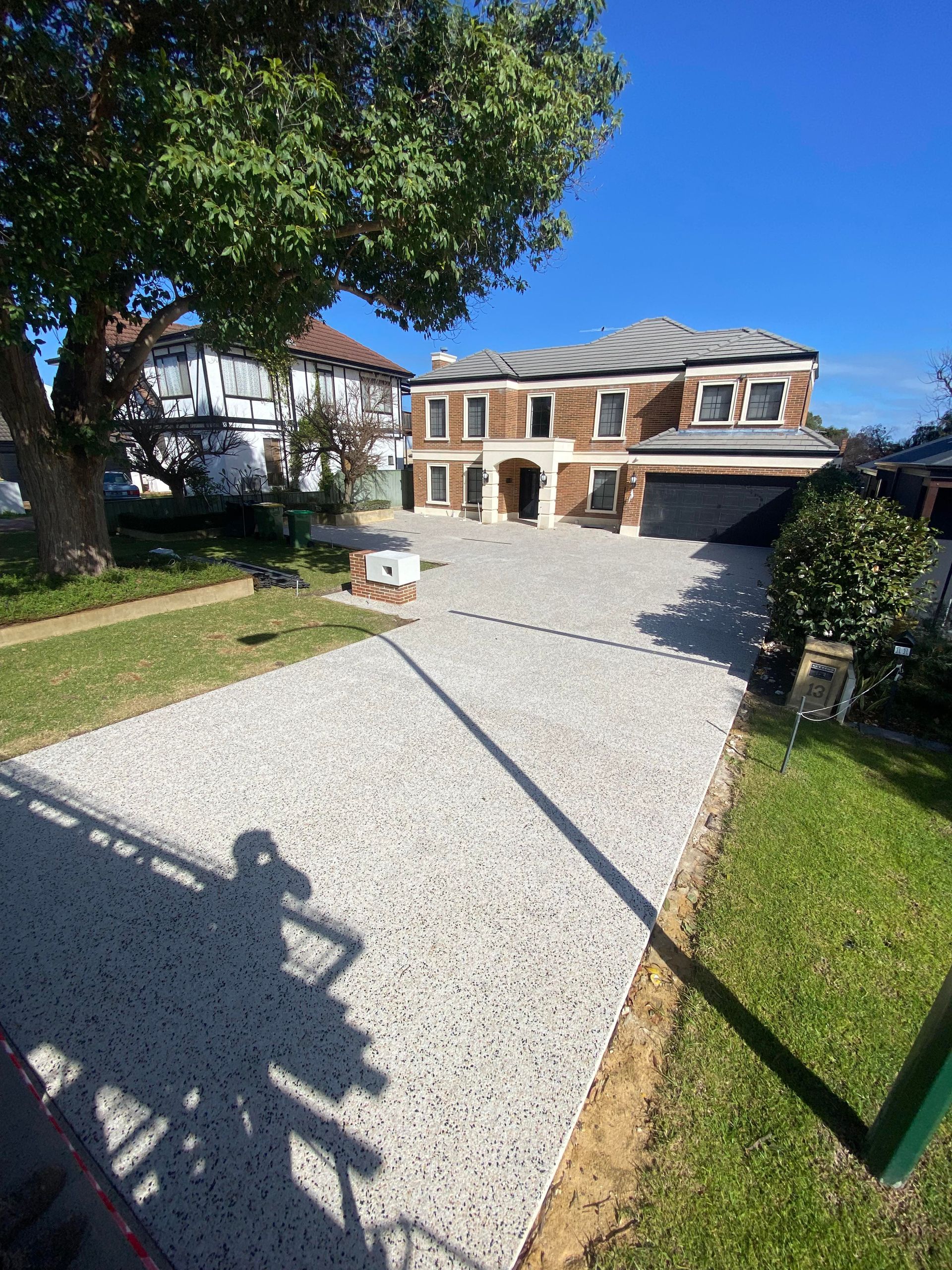 a long exposed agg driveway leading to a two storey home with gardens. 
