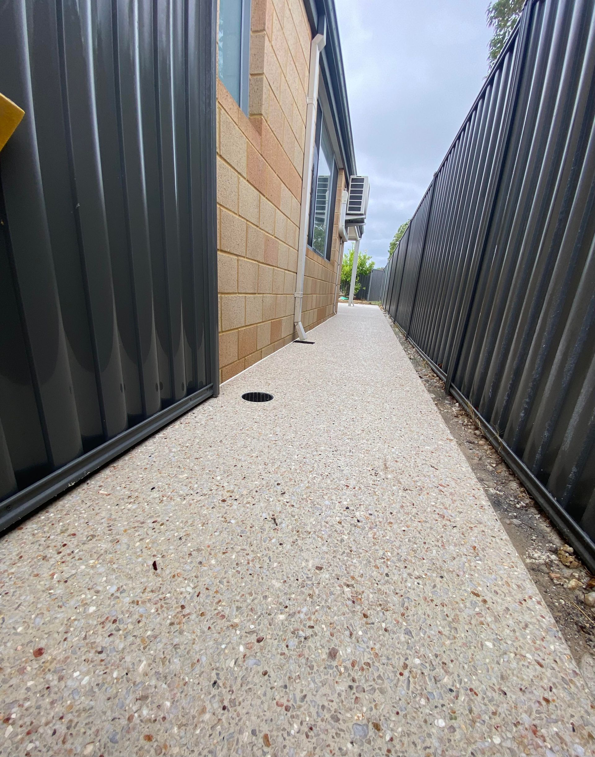 White exposed aggregate concrete pathway leading down the side of the house with black fencing.