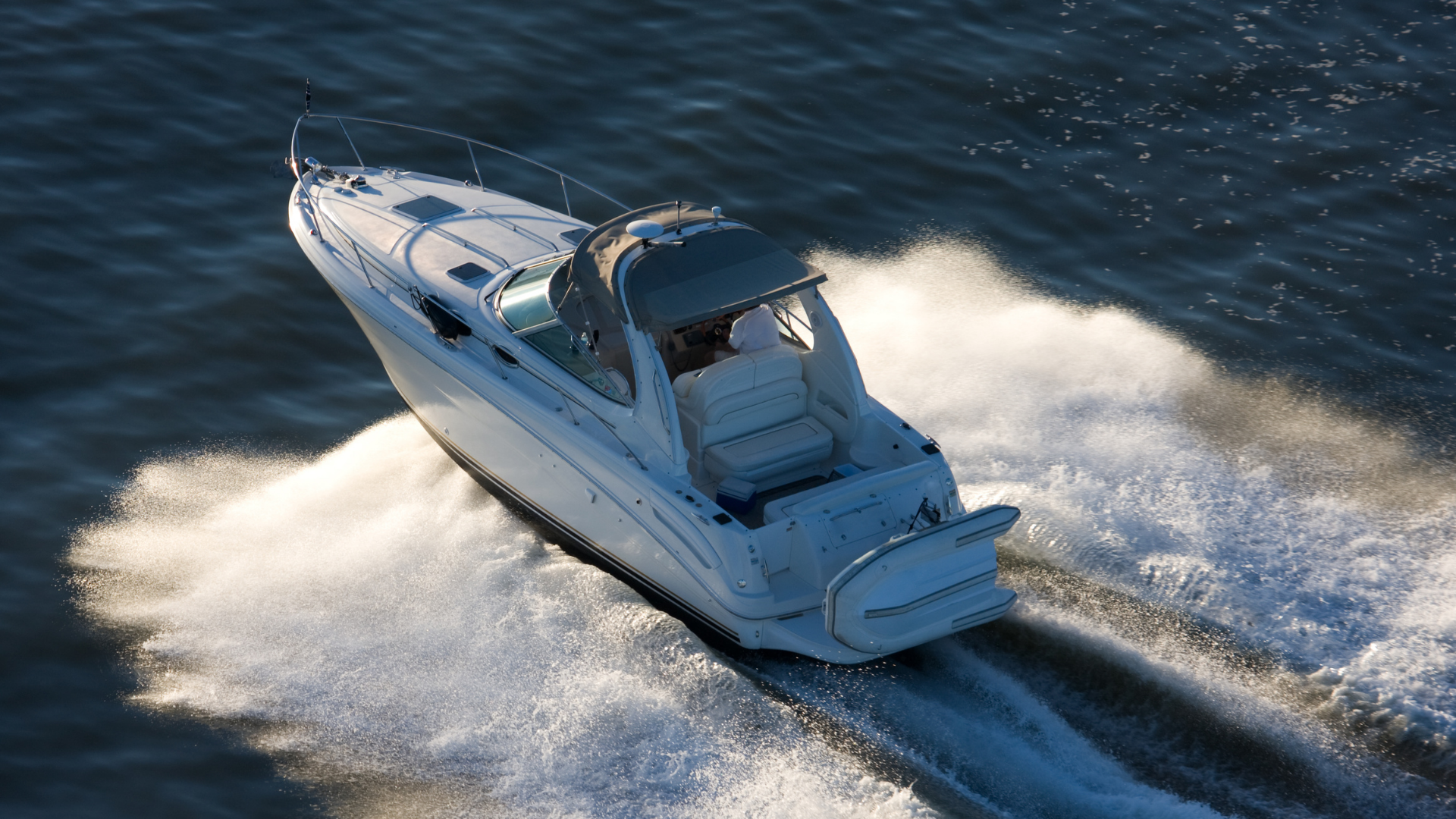 A white motorboat speeds across blue water, creating a large, foamy wake behind it.