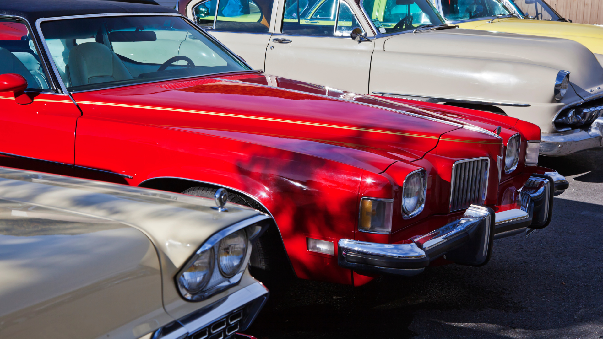A row of parked classic American cars, featuring a vibrant red vehicle in the center and light-colored cars on either side.