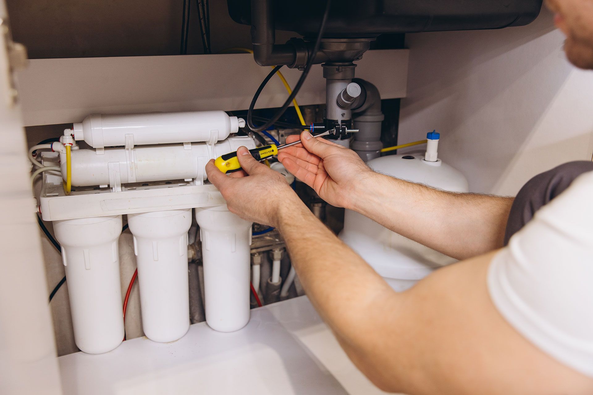 Water Softeners - Plumber Installing Water Filter System Under Kitchen Sink
