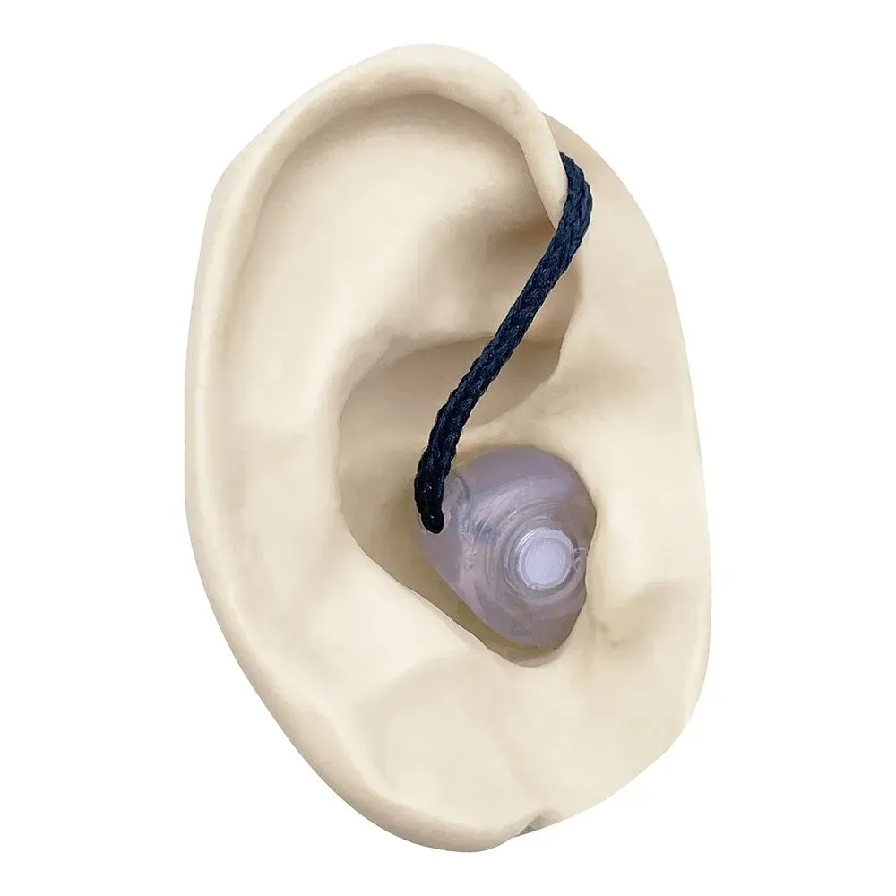 An in-ear hearing aid with a black pull-cord, shown positioned inside a beige ear model.