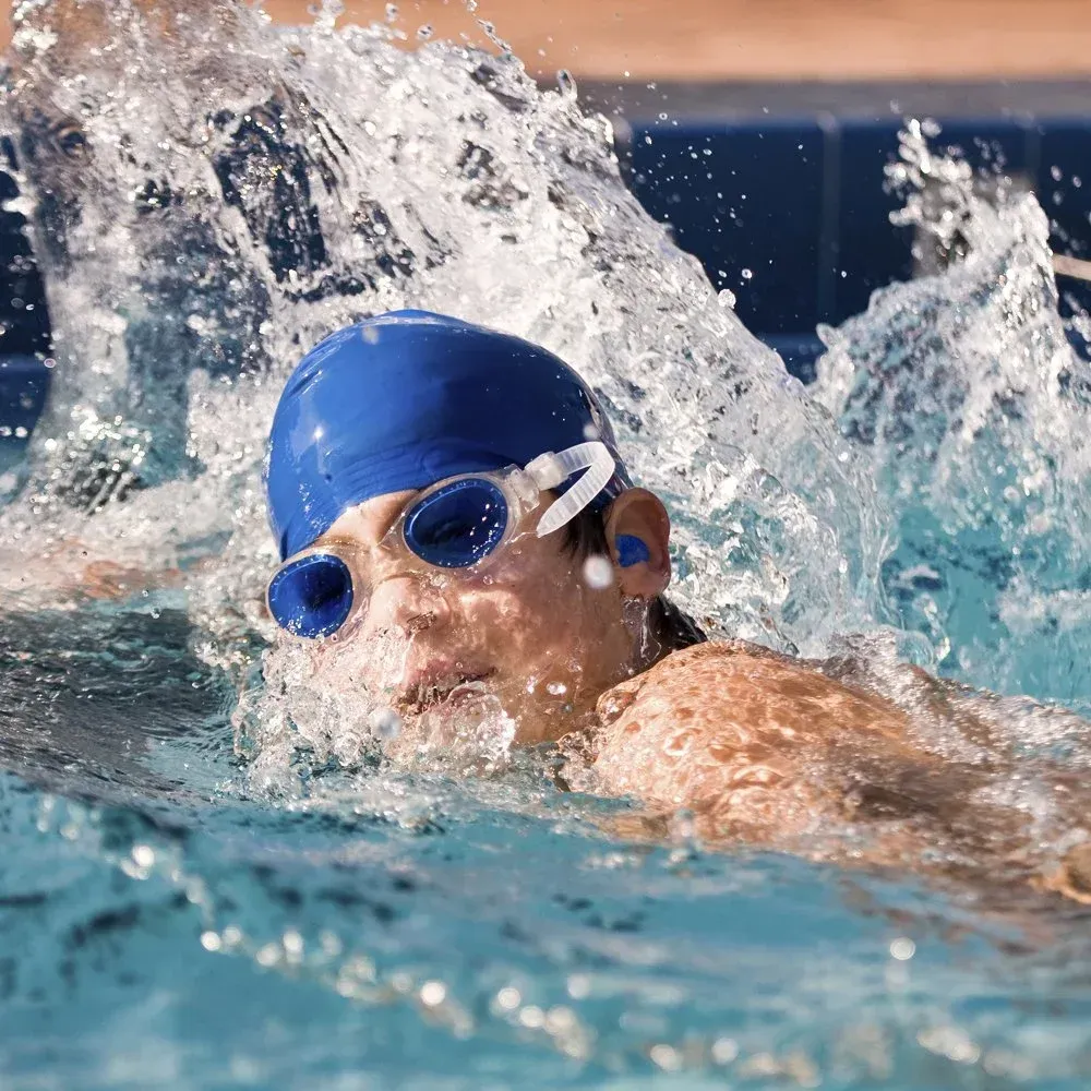 Swimmer in blue cap and goggles doing freestyle, splashing through a pool lane