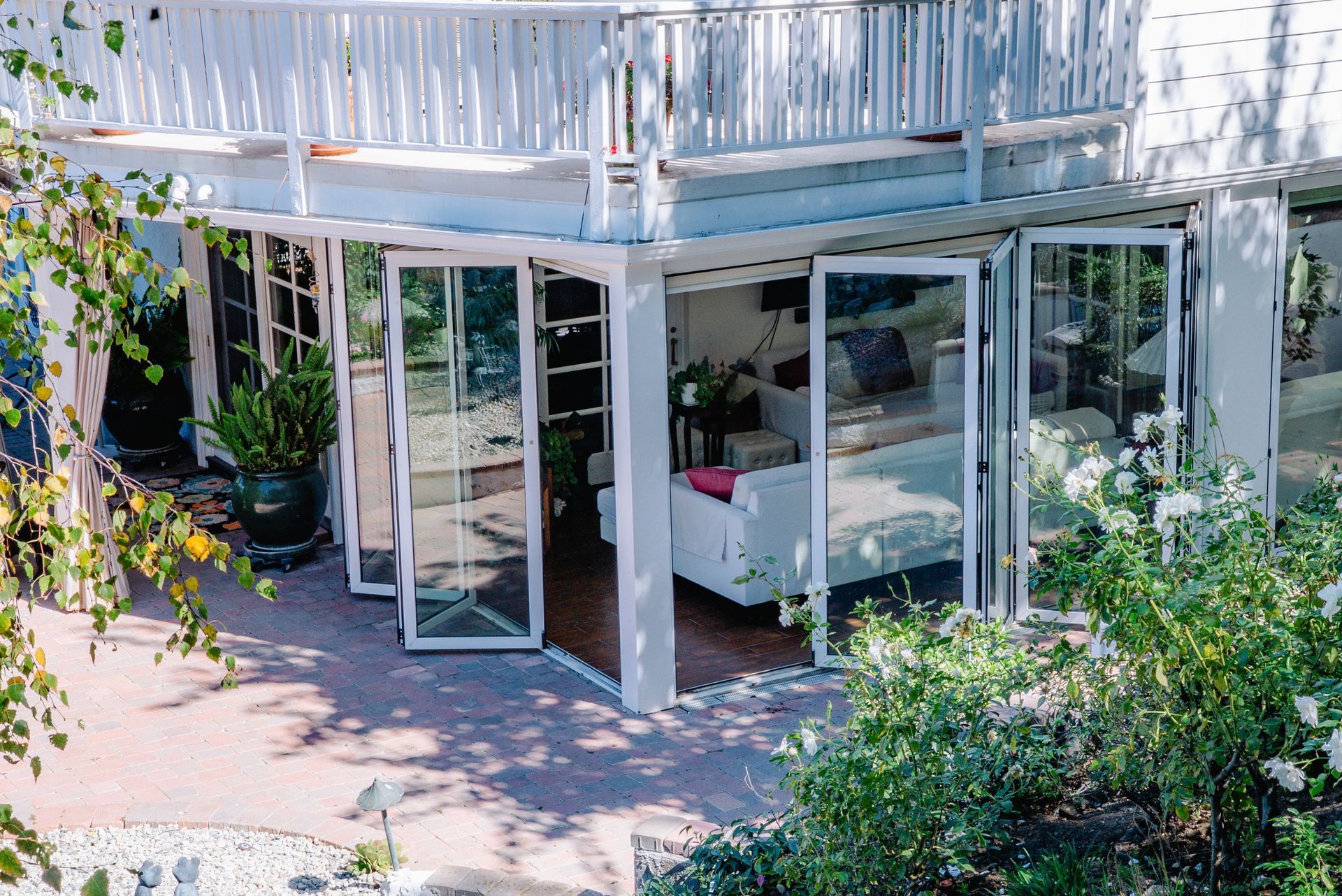 White house with balcony, glass folding doors open to outdoor patio and garden.