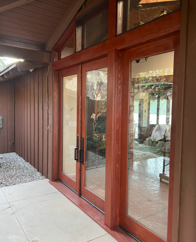 Wooden doors with glass panels, on a porch with stone and brown siding.