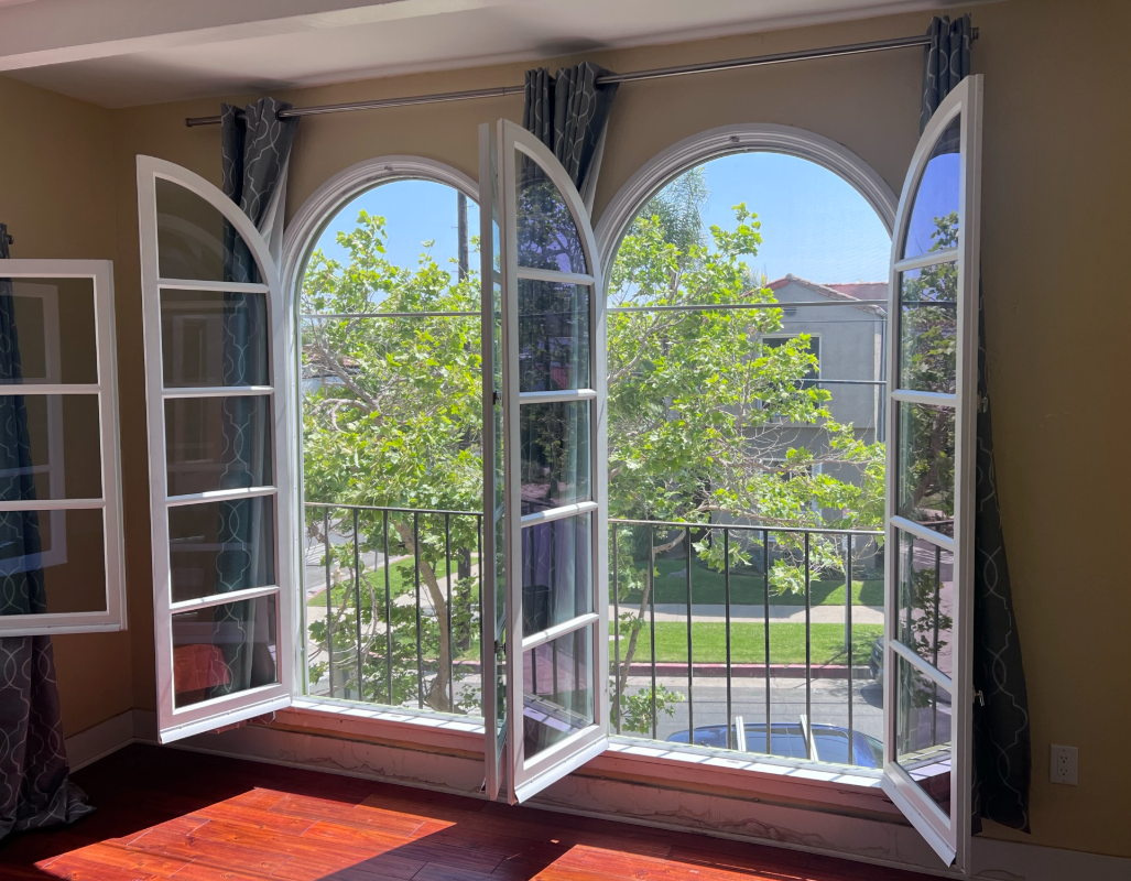 Window with burgundy trim reflecting trees, set in a yellow stucco wall.
