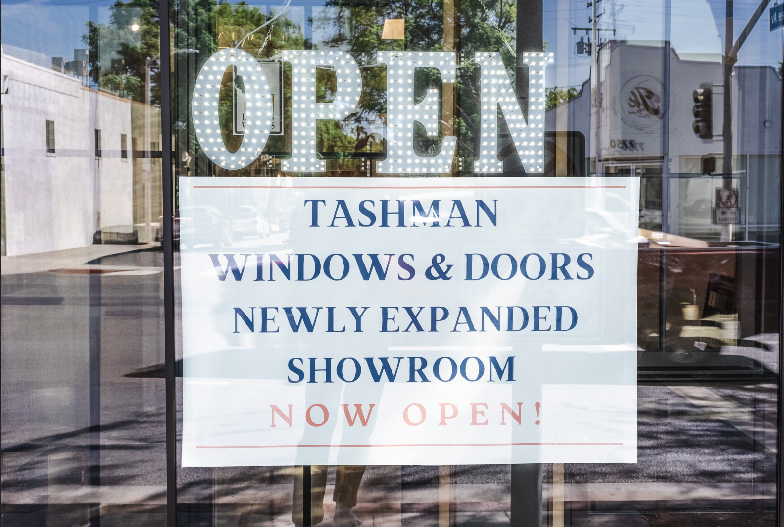 Sign on a window: “OPEN” with Tashman Windows & Doors “NEWLY EXPANDED SHOWROOM NOW OPEN!”