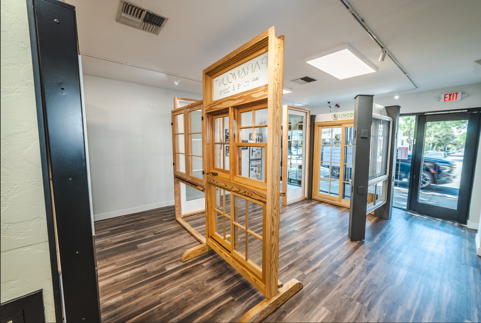 Wooden window display in a showroom with wood-look floors and neutral walls, showcasing various window styles.