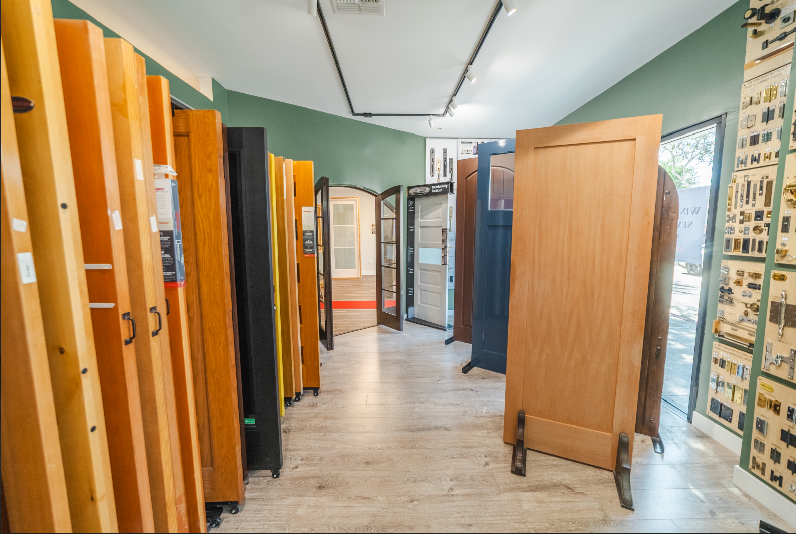 Showroom with various wooden doors on display, featuring different styles and finishes, with a green wall and track lighting.