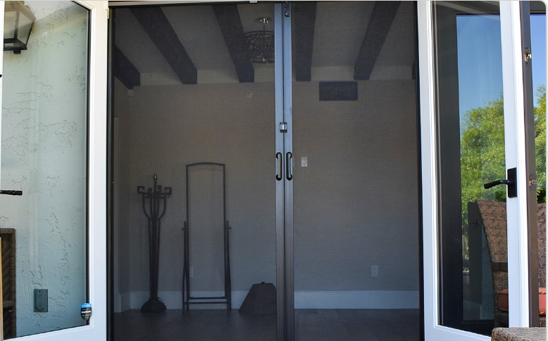Double-door screen door, dark gray mesh, leading into a room with white walls and wooden beams.