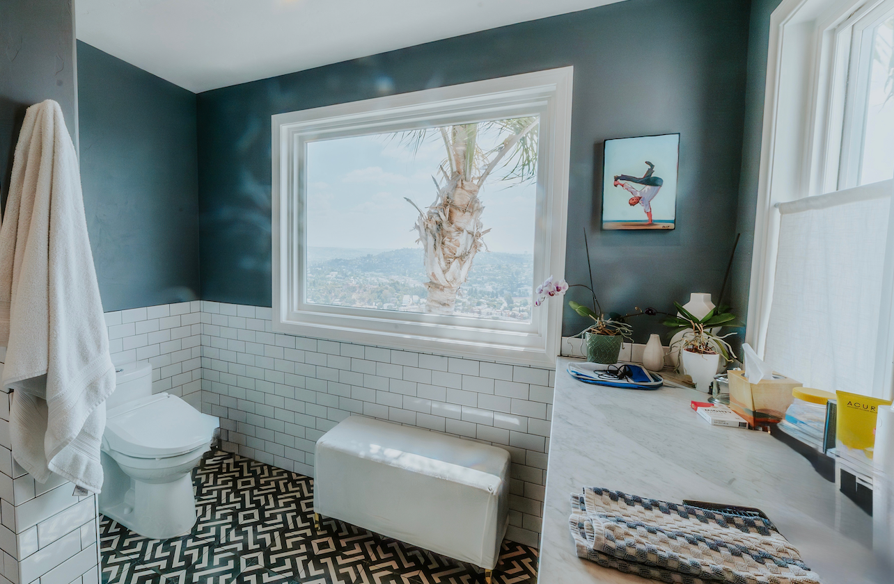 Bathroom with blue walls, white window and trim, white toilet, and patterned floor.
