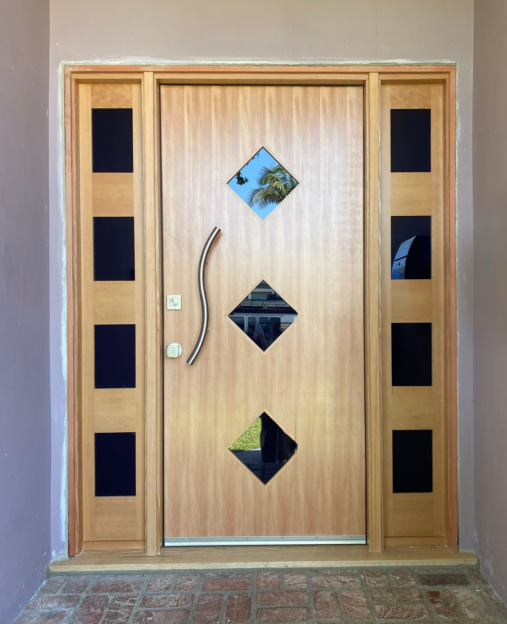 Wooden front door with diamond glass panes and side windows, framed by beige walls.