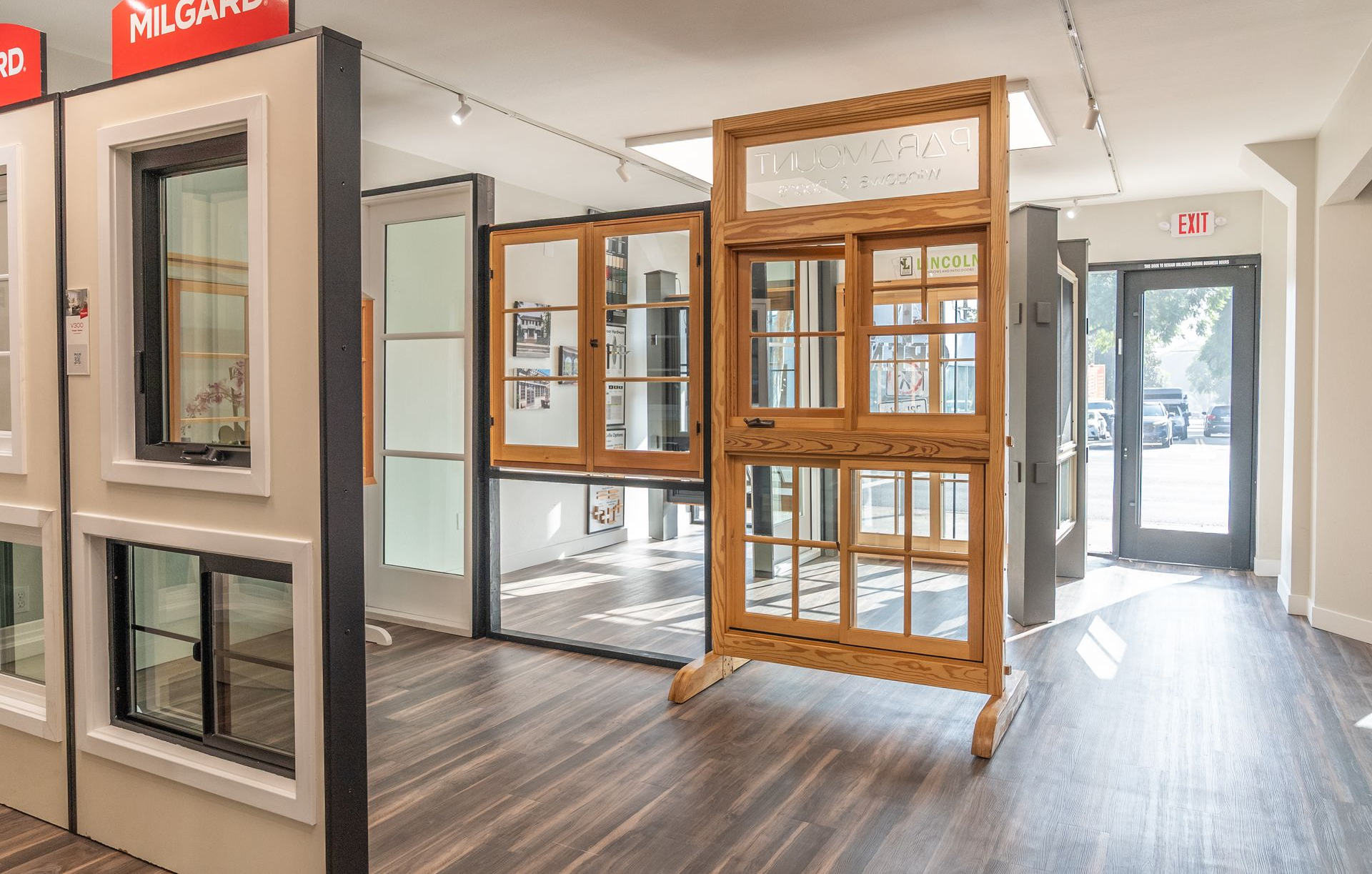 Showroom with window displays, light wood and white frames, dark wood flooring, bright lighting.
