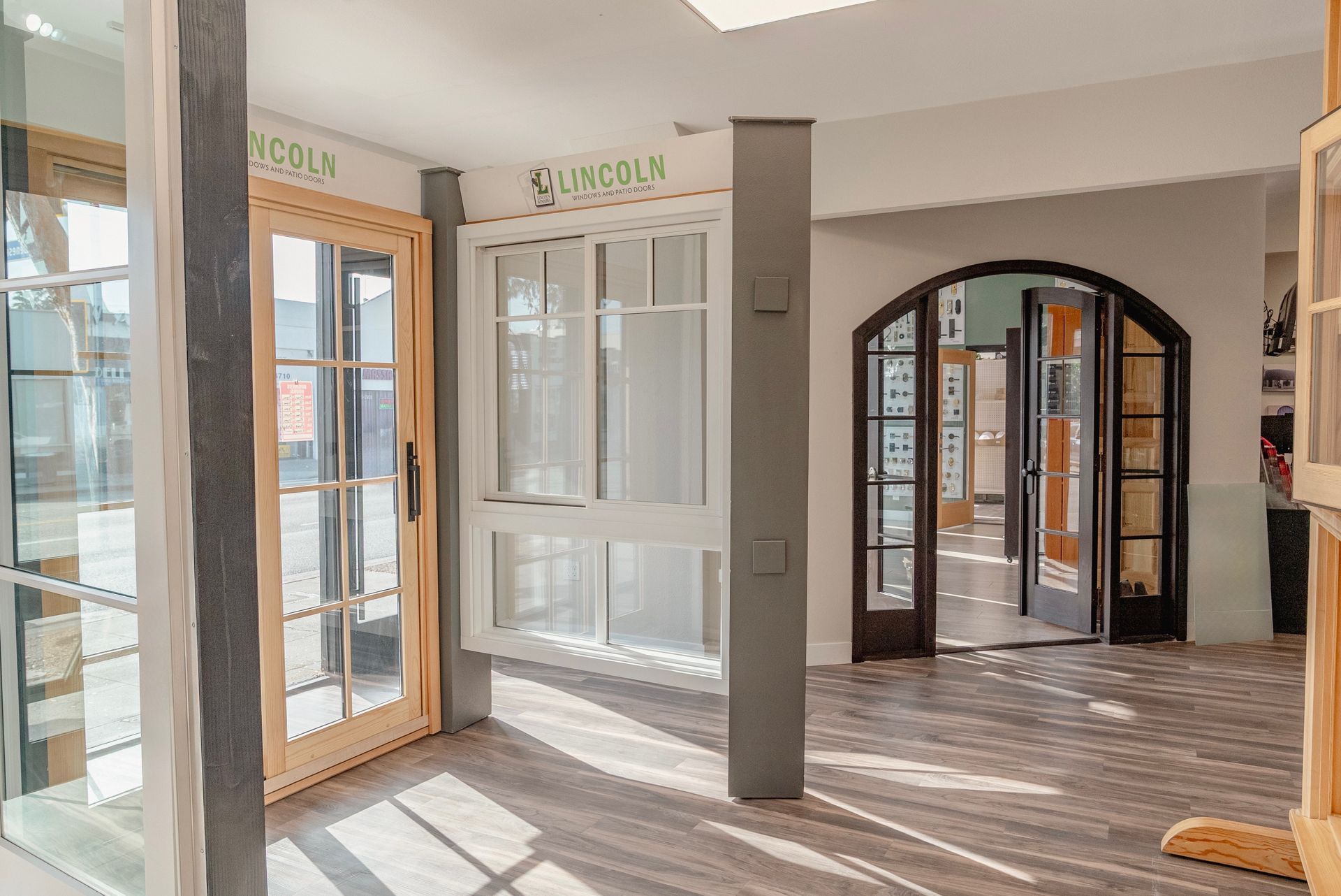 Interior of a window and door showroom with displayed samples and an archway leading to another room.