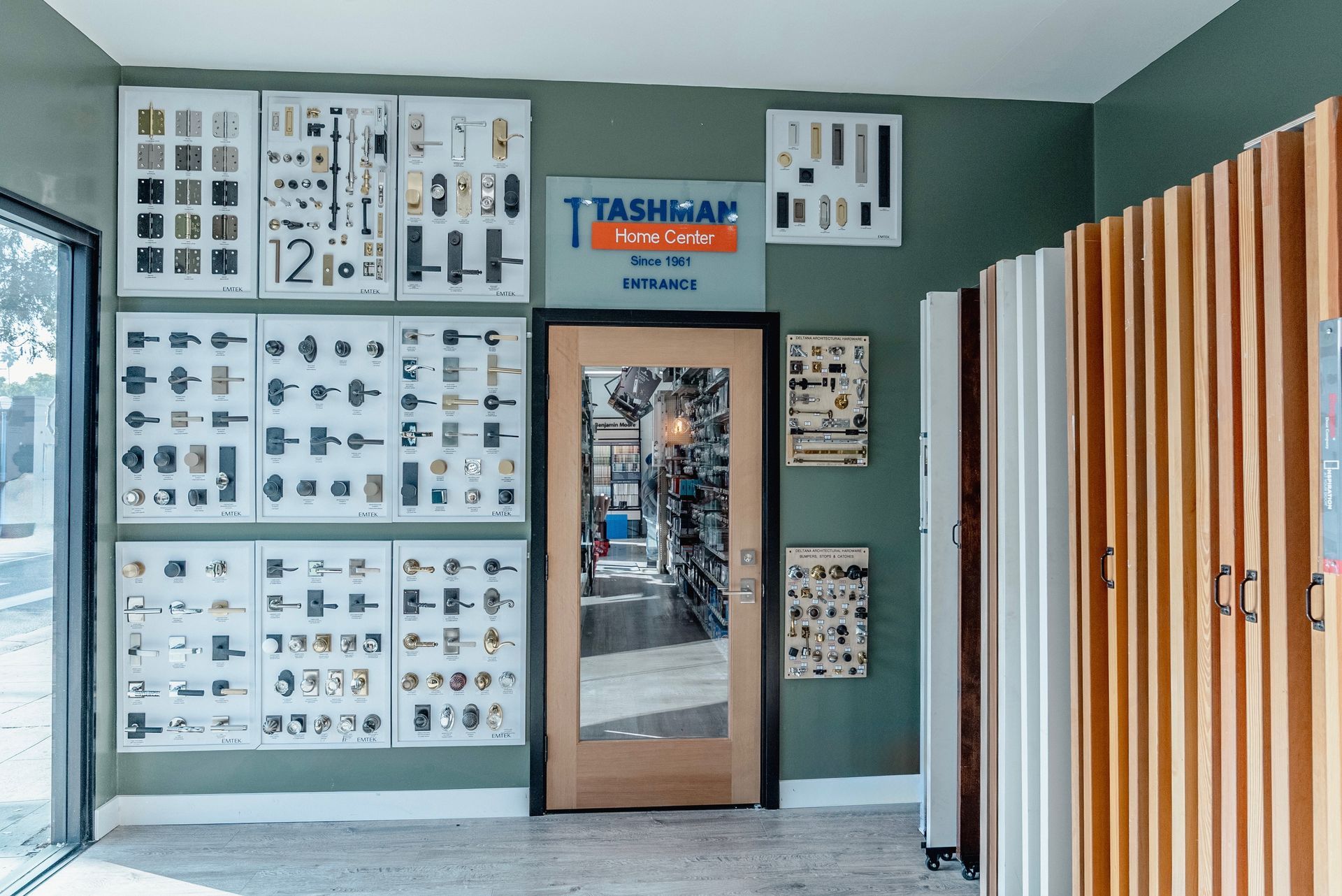 Interior of a store with door hardware displays on green wall, entrance in the center.