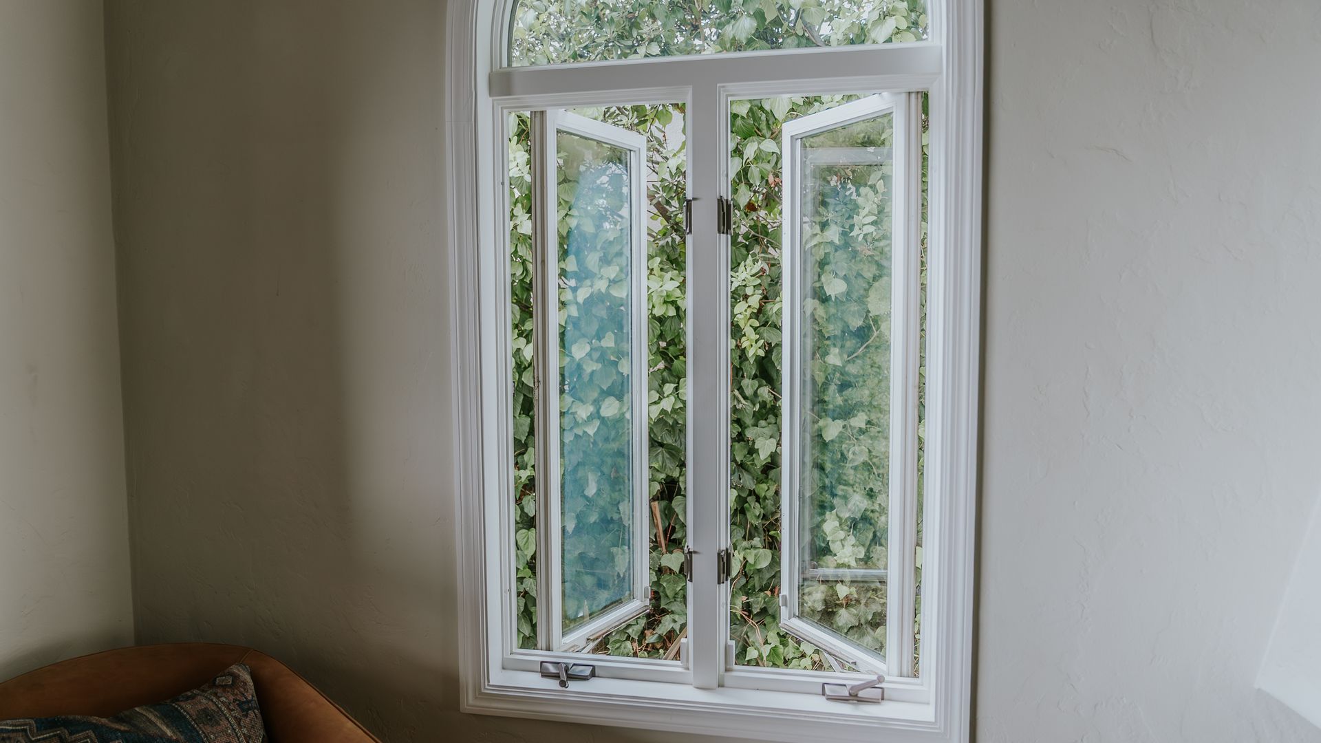 Open arched windows with white frames, overlooking greenery and a balcony.