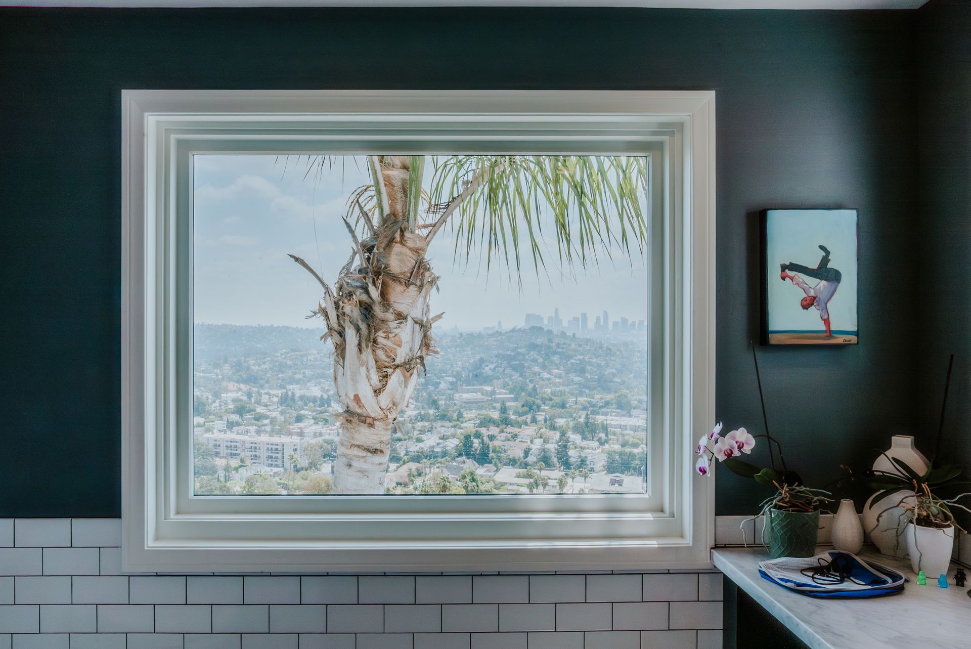 Black-framed window with view of trees and buildings, set in a light-colored wall, a couch is in the corner.
