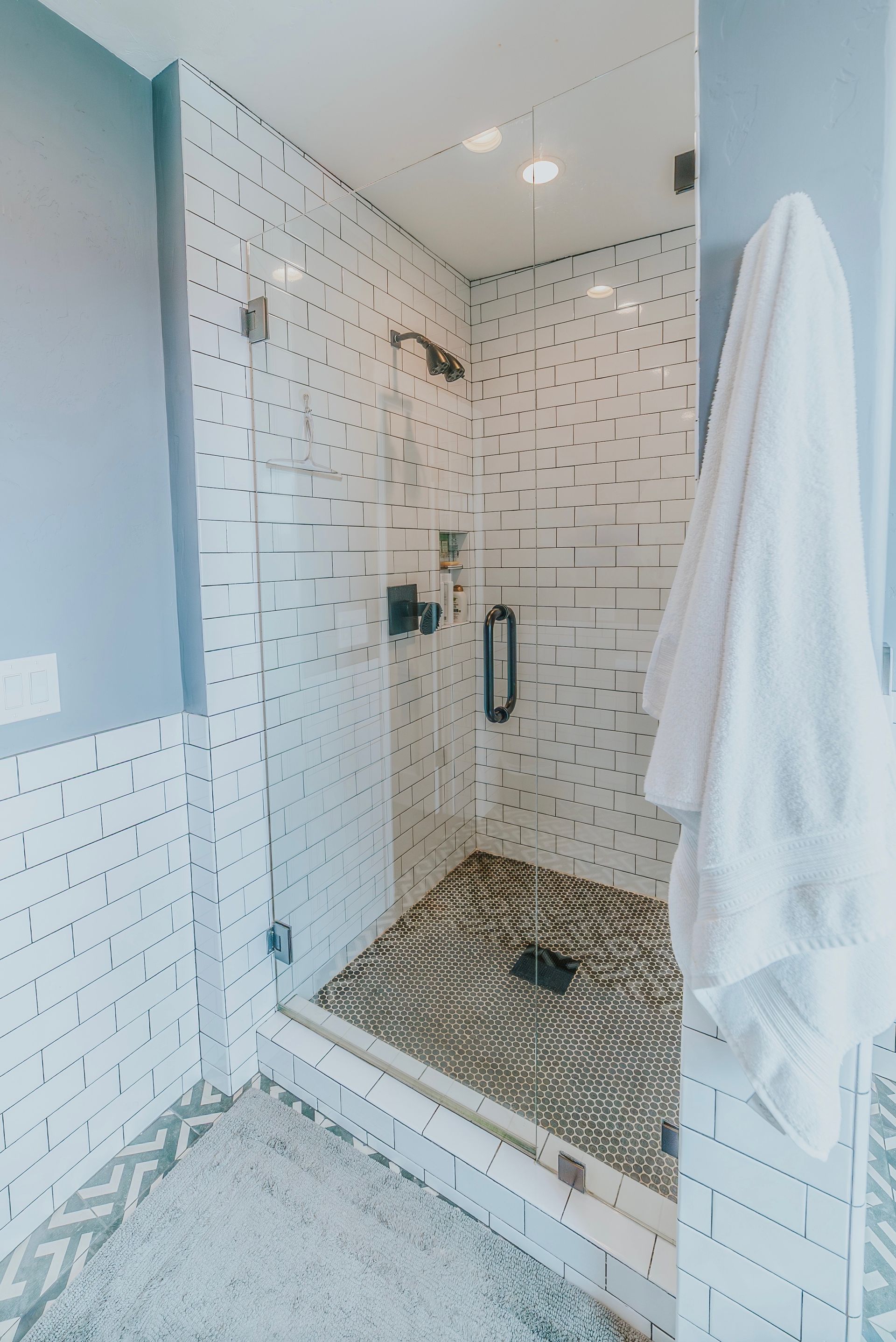Shower with black and white speckled tile walls, glass door, and a white towel.