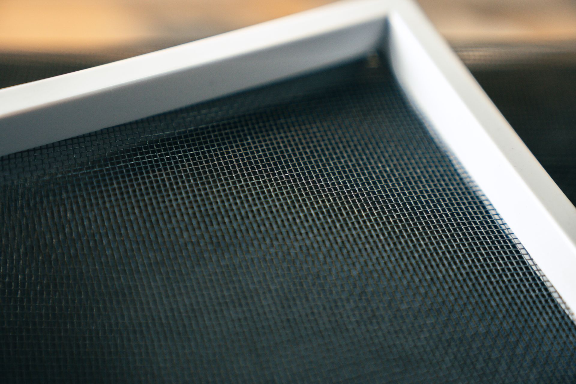 Close-up of a white-framed black screen, showing woven mesh, likely a window or door screen.