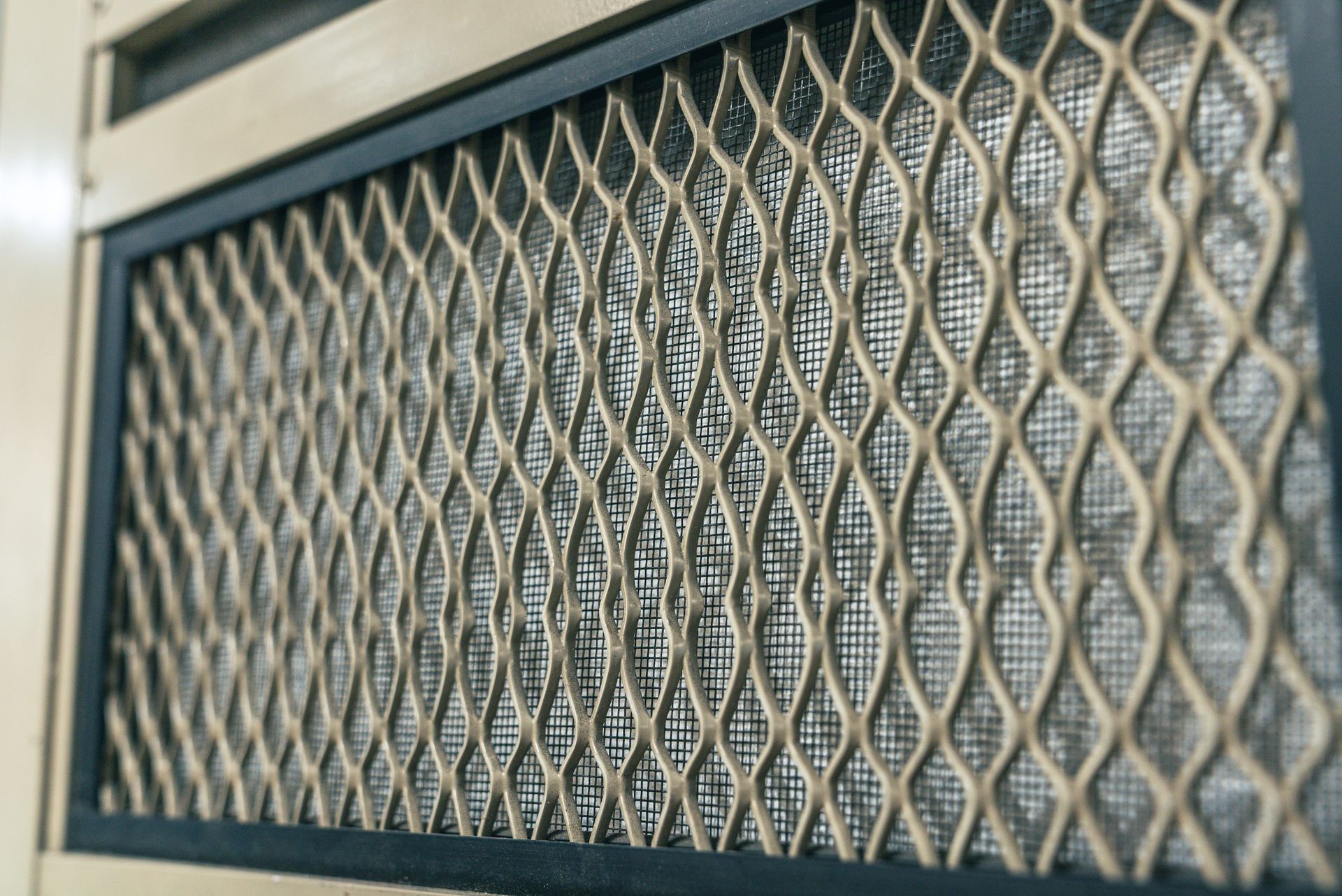 Close-up of a metal security door with diamond-patterned grill over a mesh screen.