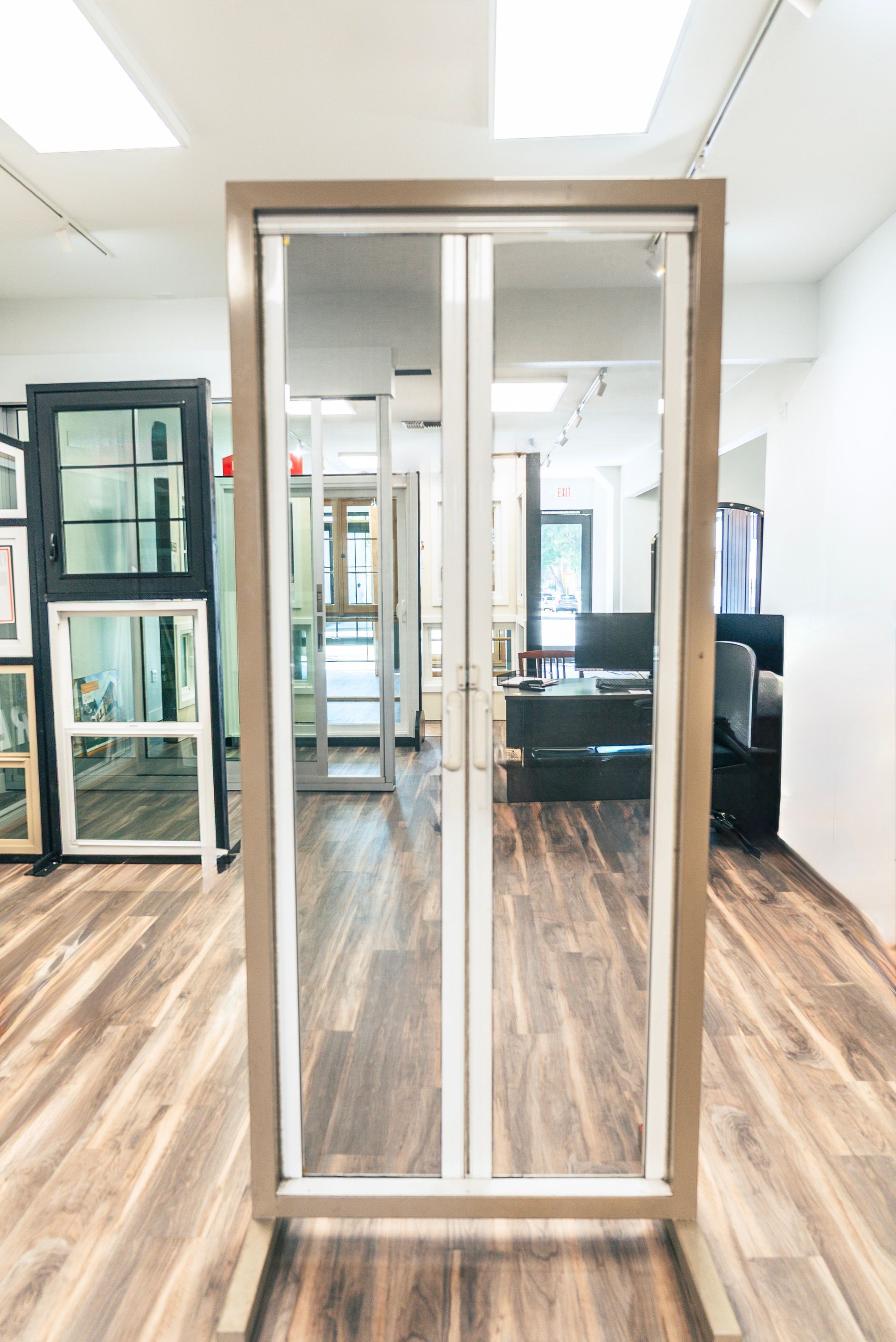 Two-door glass display in a showroom, wooden floor, tan frame, white dividers.