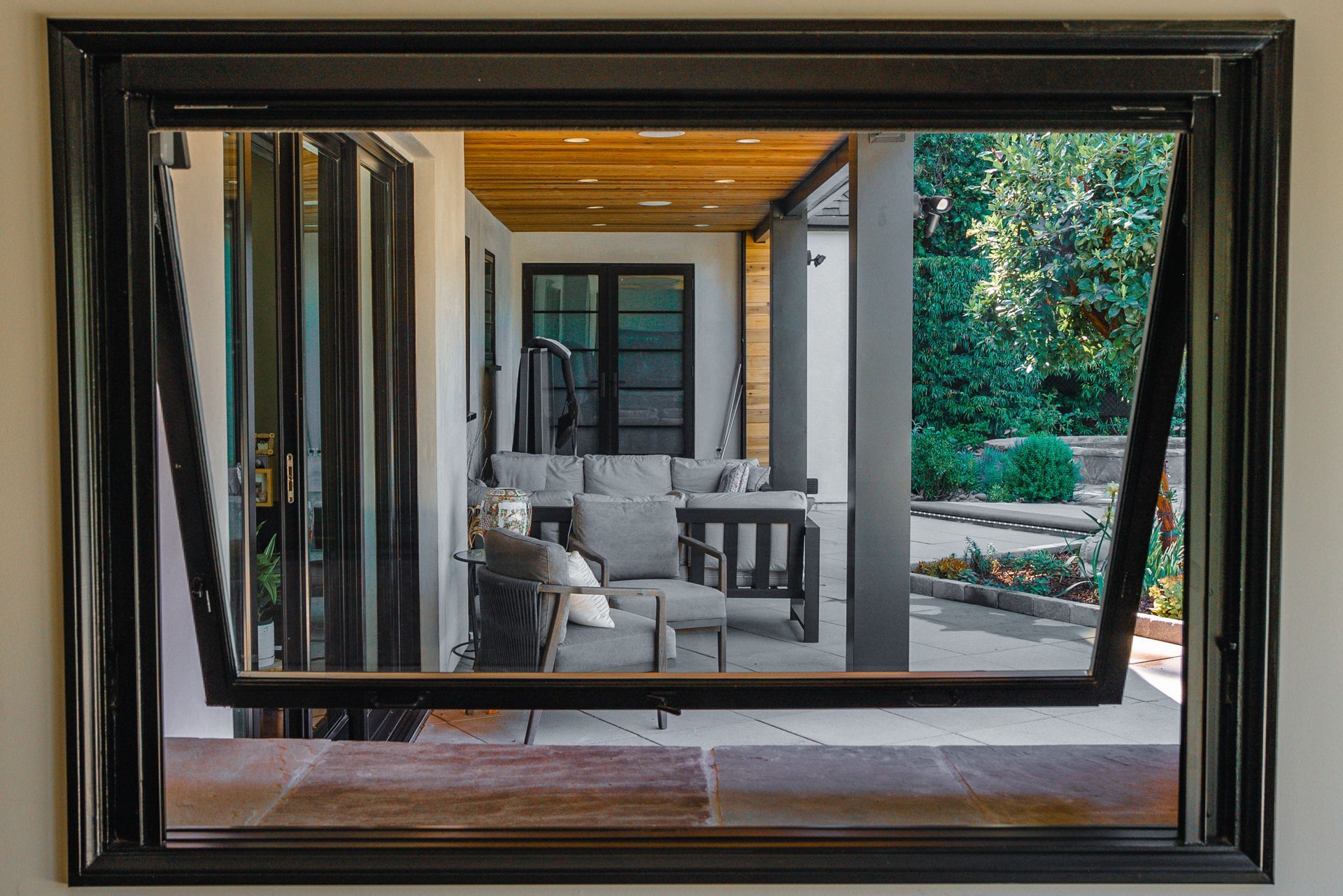 Framed view of a covered patio with seating, wood ceiling, and garden beyond